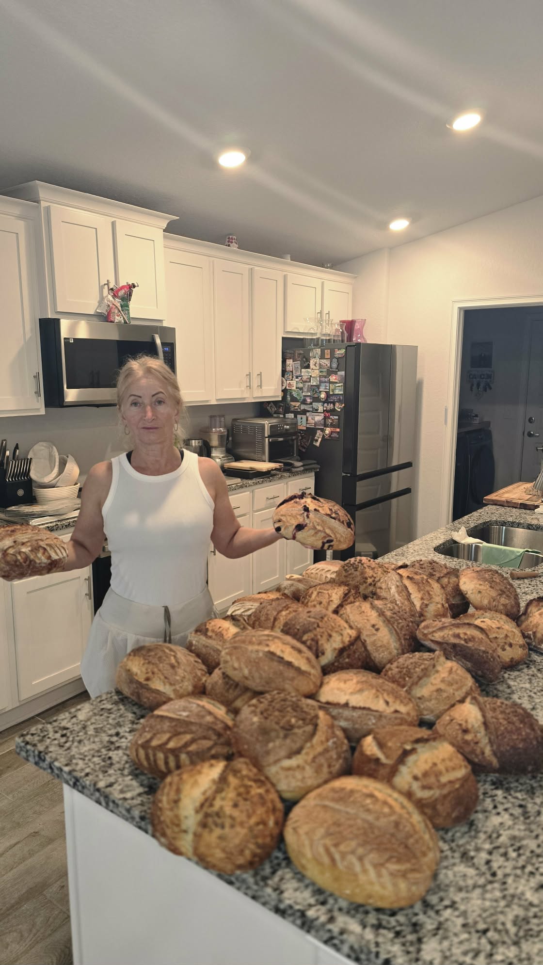 Eva in her home kitchen with a large batch of sourdough loaves baked from this starter.